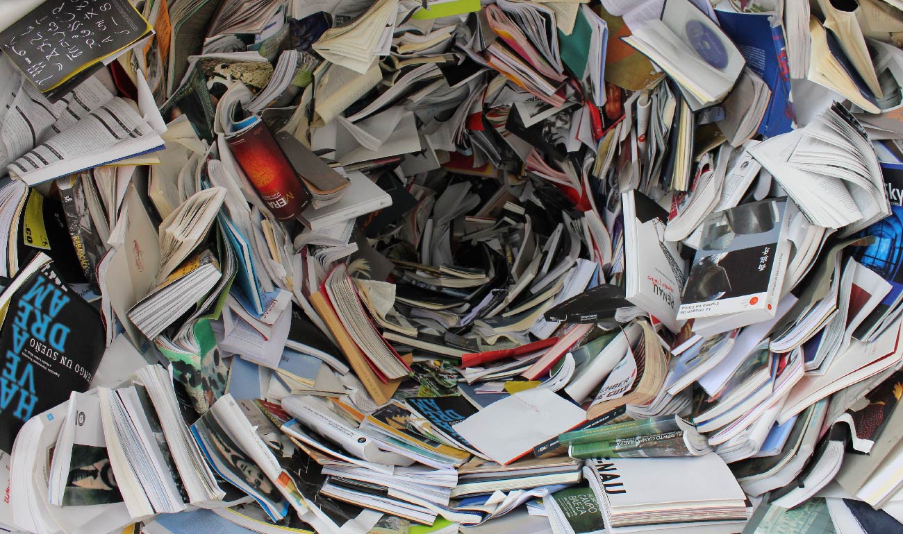 Fotografía superior de una figura hecha con libros y revistas. Da la sensación de estar viendo embudo. 
