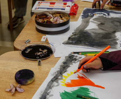 Fotografía de una mesa con implementos de dibujo y niños pintando