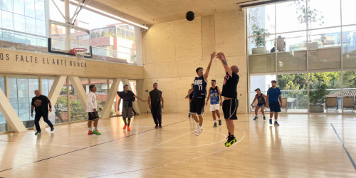 Fotografía de grupo de personas jugando baloncesto en la cancha de la arena polivalente